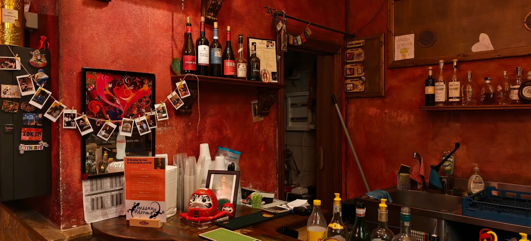 Bottiglie, fotografie e oggetti sul bancone rosso